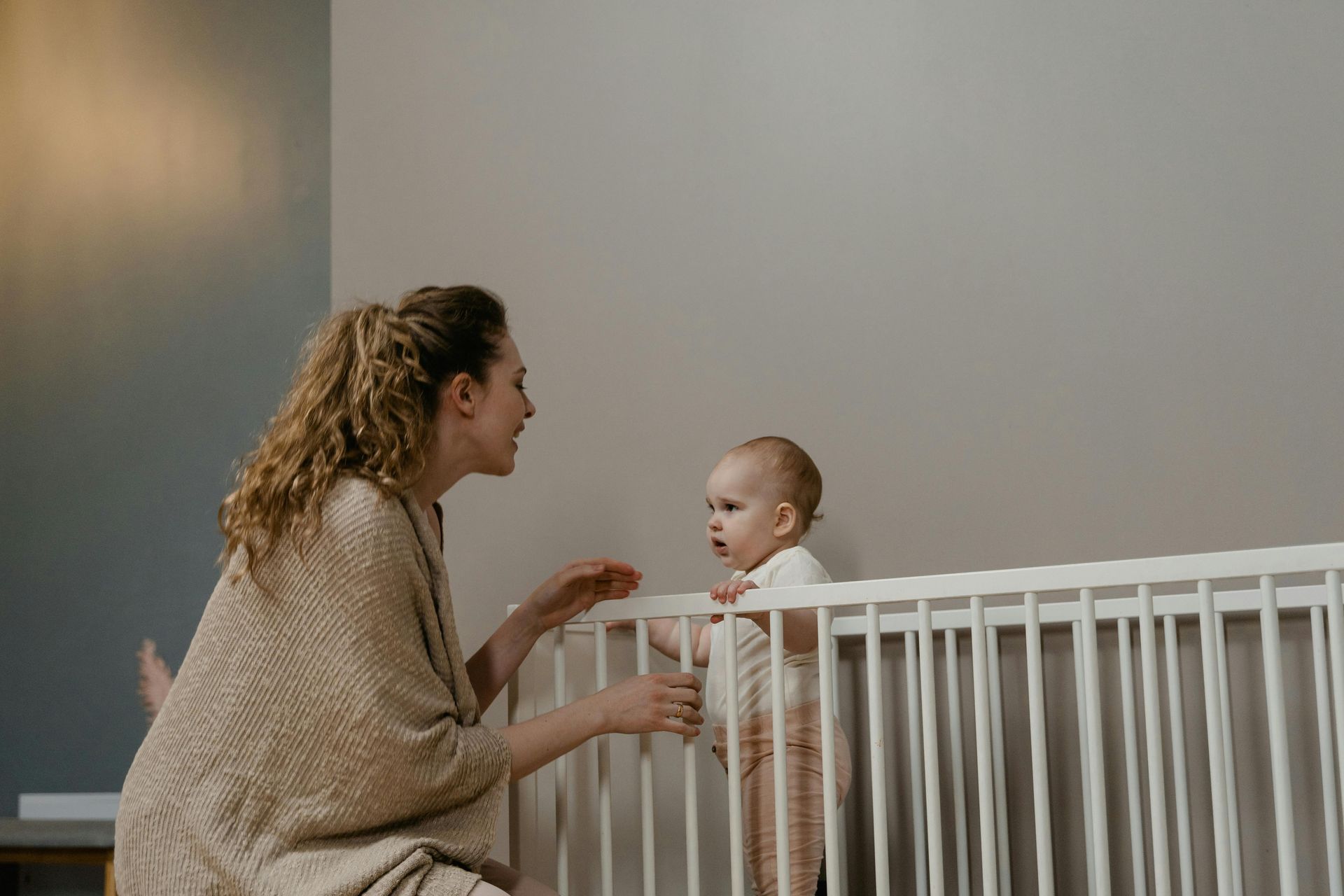 A woman is sitting next to a baby in a crib.