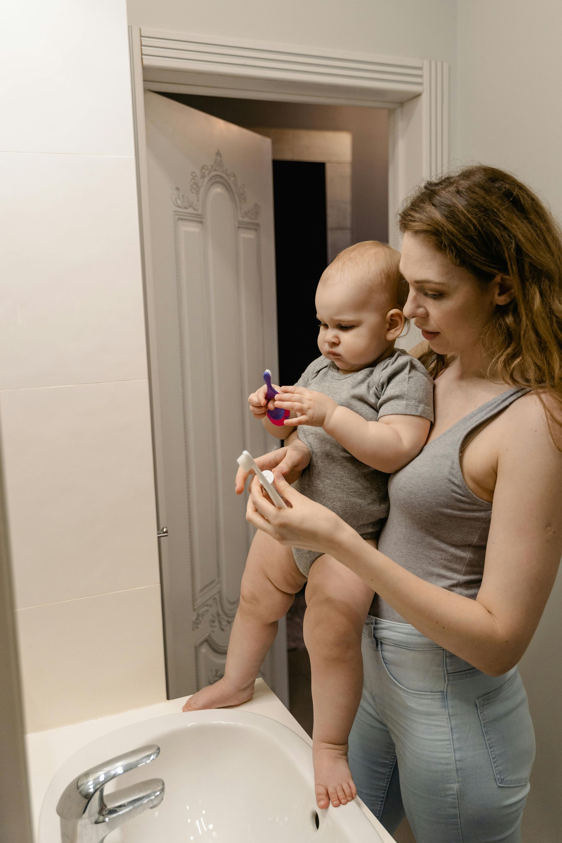 Woman holding baby in bathroom, showing how to brush teeth.