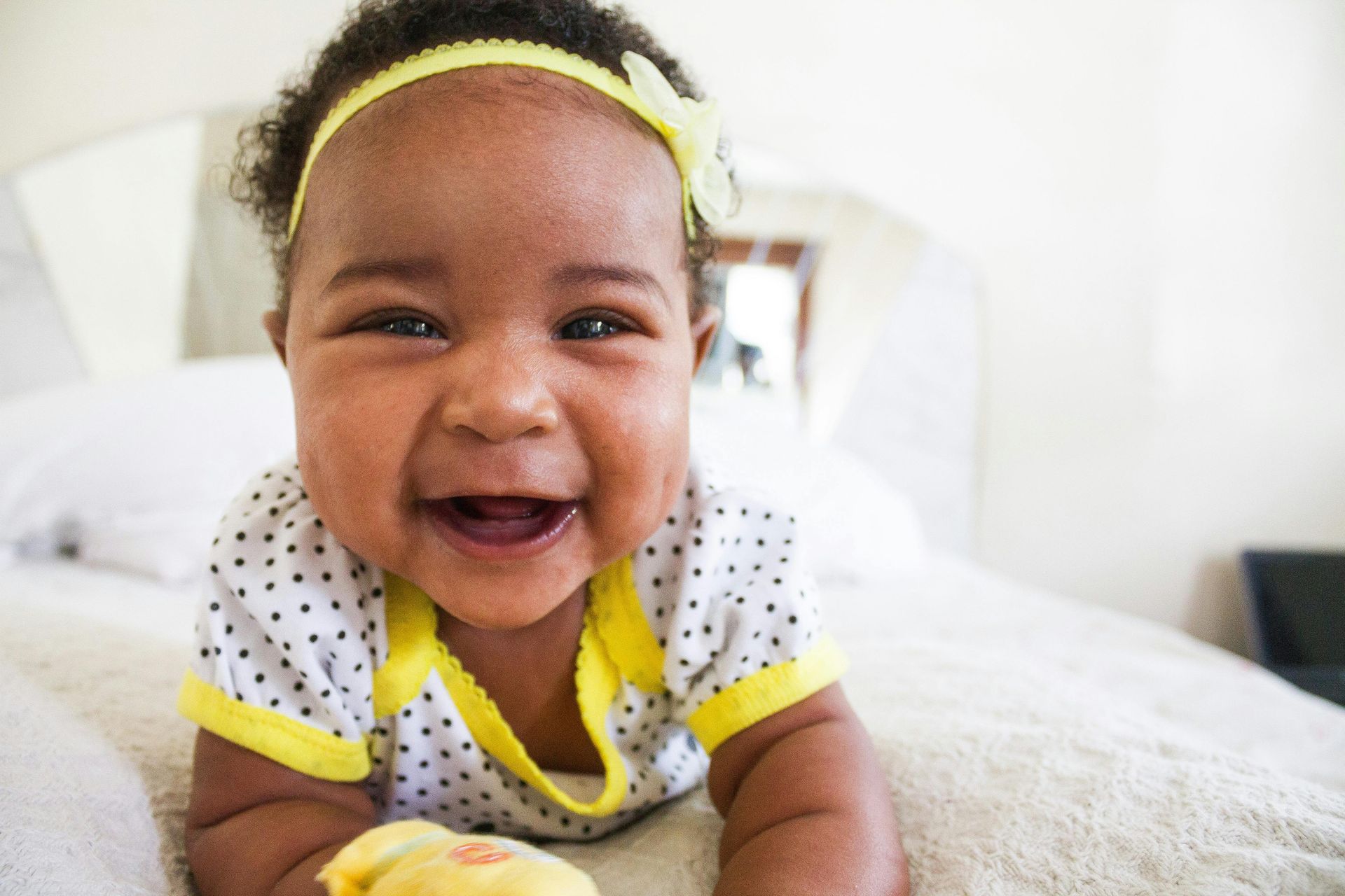 A baby is laying on her stomach on a bed and smiling.