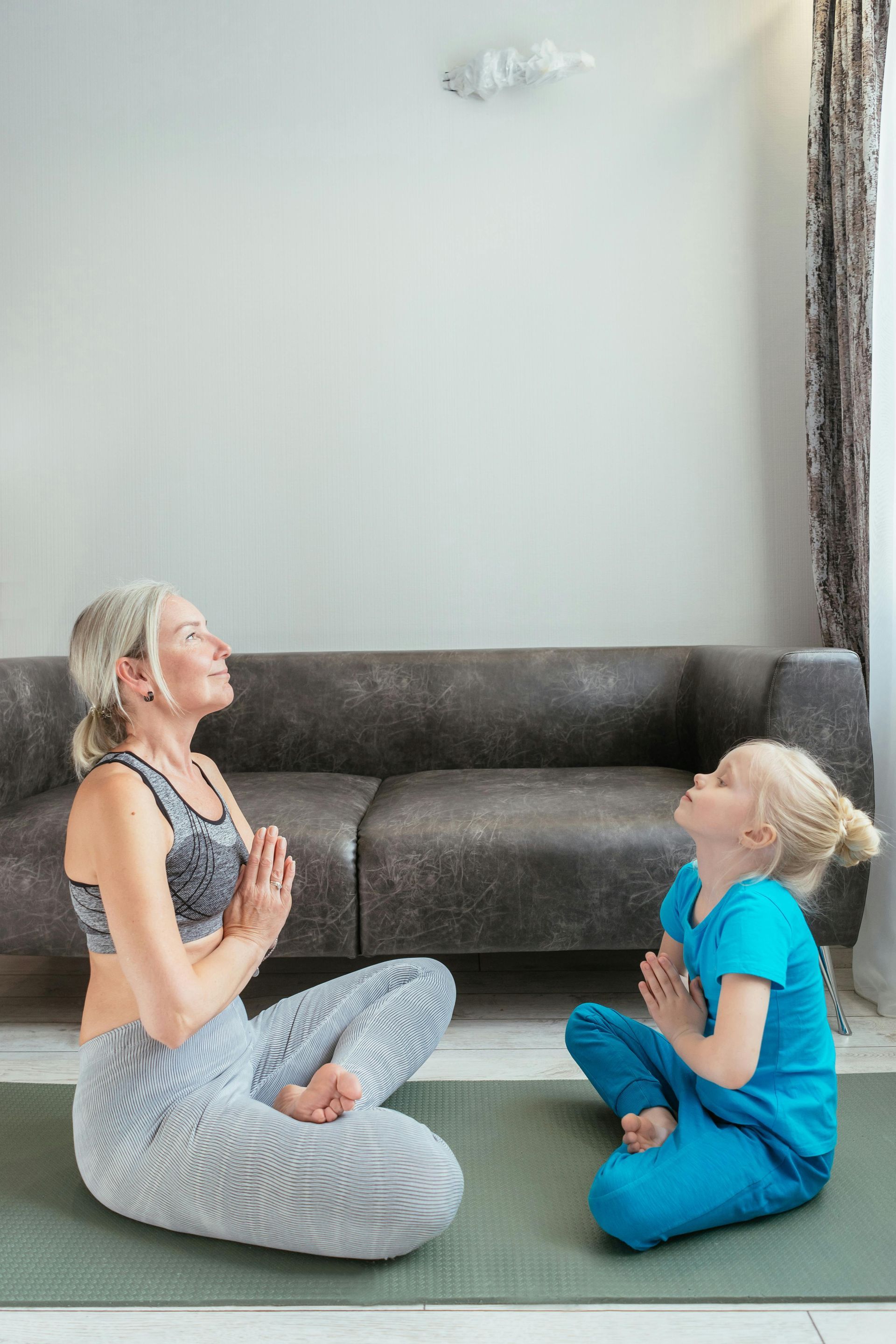 A woman and a child are sitting on a yoga mat in a living room.