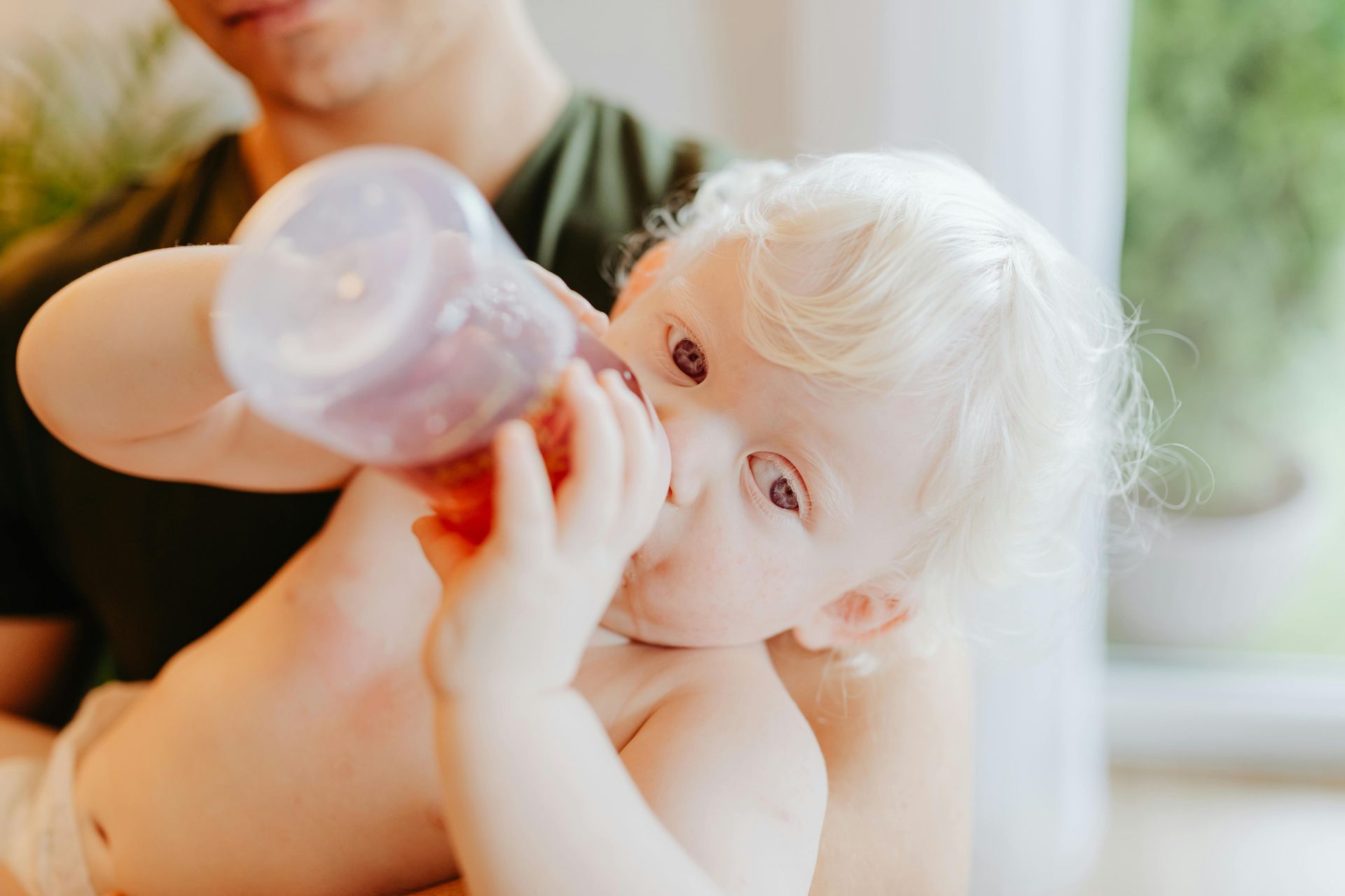 A baby is drinking from a bottle while being held by a man.