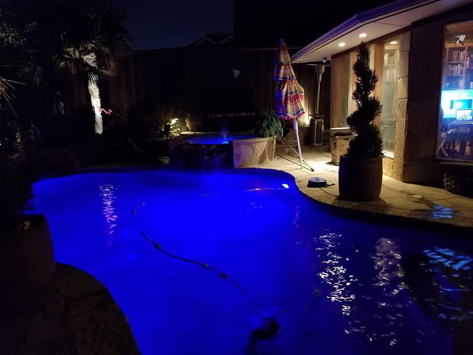 A large swimming pool is lit up with blue lights at night.