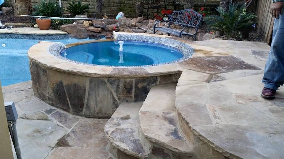 A man is standing next to a hot tub next to a swimming pool.