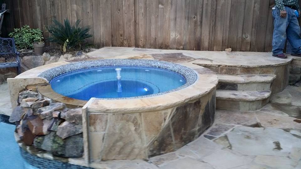A man is standing next to a hot tub next to a pool.