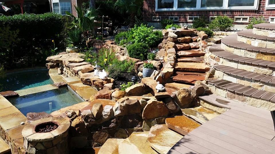 A swimming pool surrounded by rocks and stairs in a backyard.