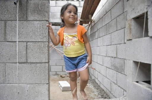 A little girl is standing next to a brick wall