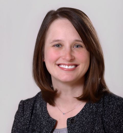 A woman wearing a black jacket and necklace smiles for the camera