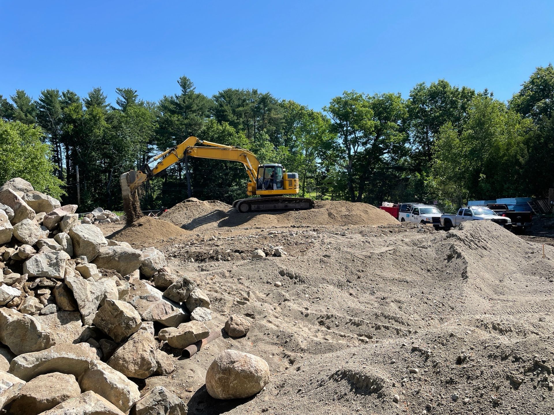 A yellow excavator is working on a pile of rocks
