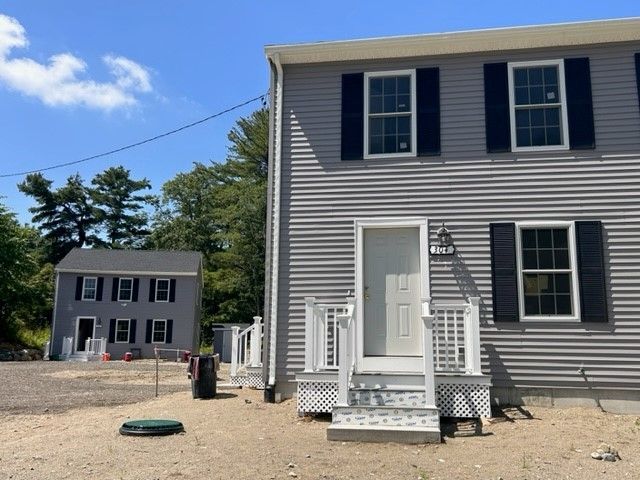 A gray house with black shutters sits next to a white house