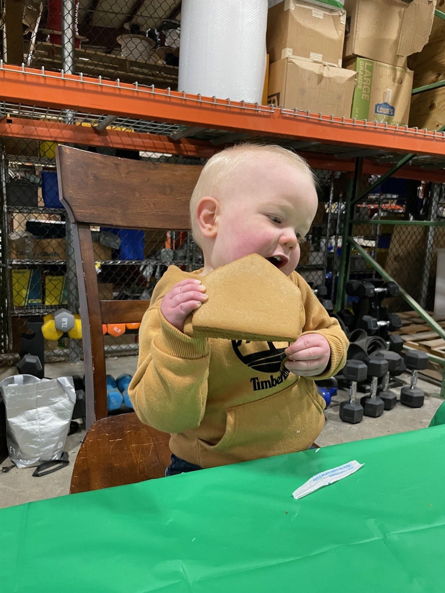 A baby wearing a timberland shirt is eating a piece of bread