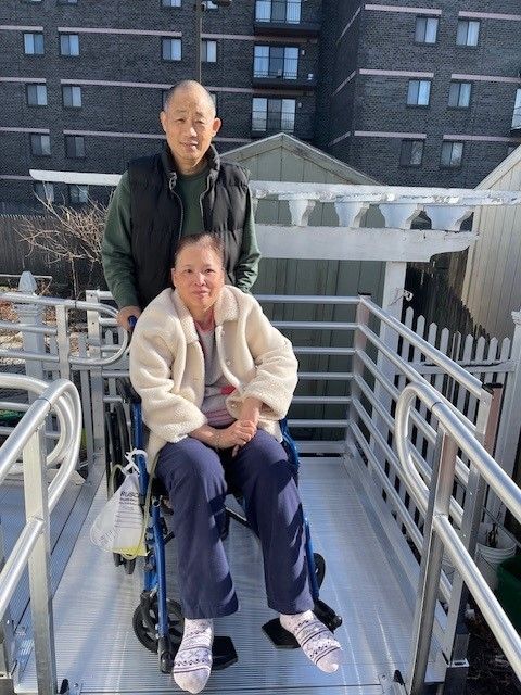 A man is standing next to a woman in a wheelchair on a ramp.