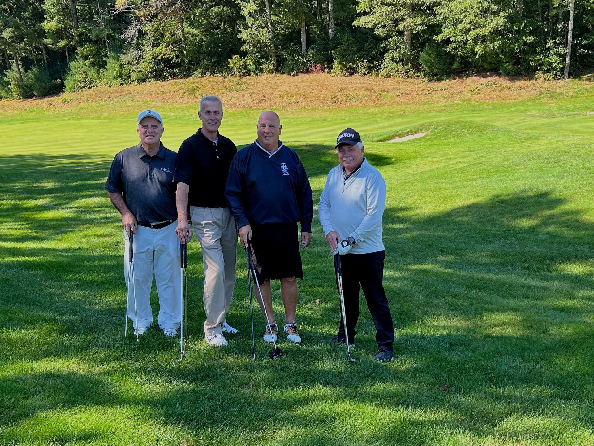 Four men standing on a golf course holding golf clubs