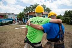 Two construction workers are hugging each other in front of a house.