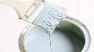 A paint brush is sitting on top of a can of white paint.