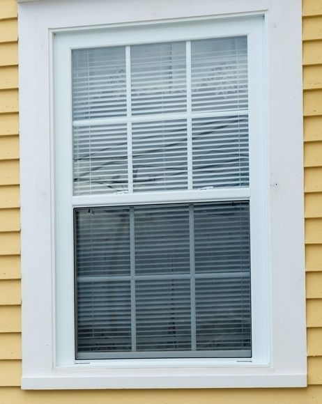 A white window with blinds on a yellow house