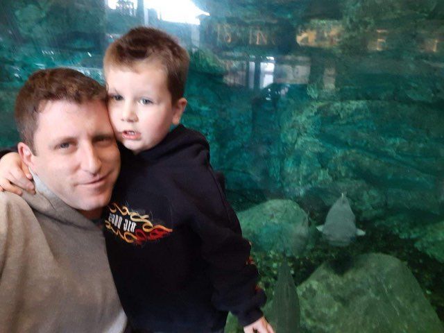 A man is holding a little boy in front of an aquarium