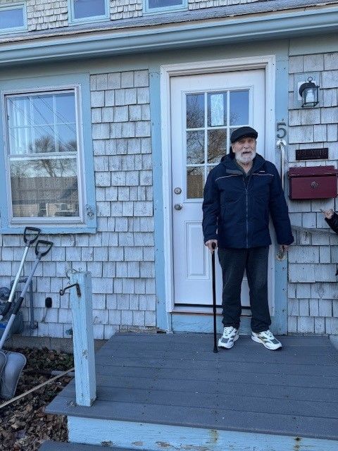 A man with a cane is standing in front of a house