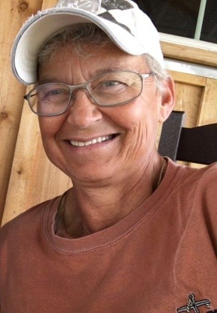 A woman wearing glasses and a hat is smiling for the camera