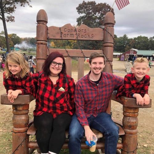 A family is posing for a picture in front of a large wooden chair that says condors farm rocks