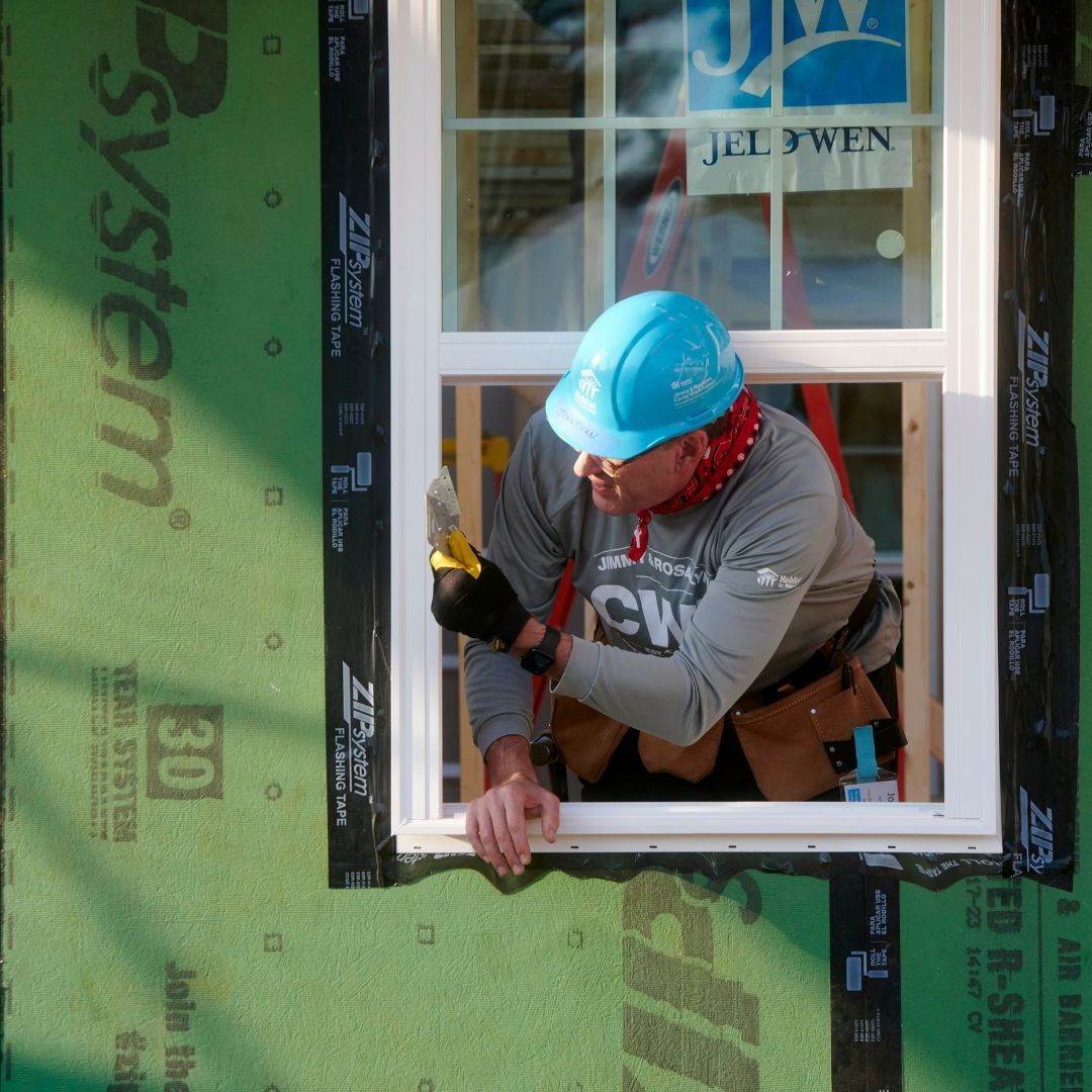 A man wearing a blue hard hat is working on a window