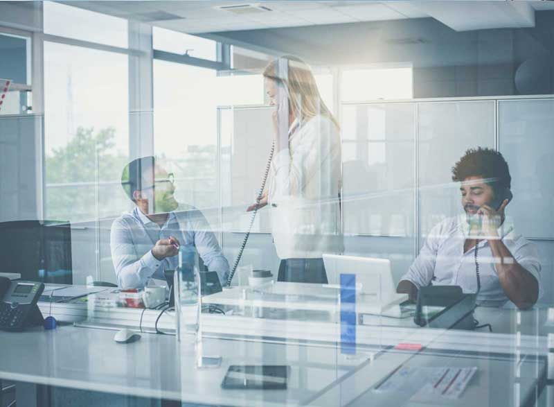 a group of people are sitting at desks in an office talking on phones .