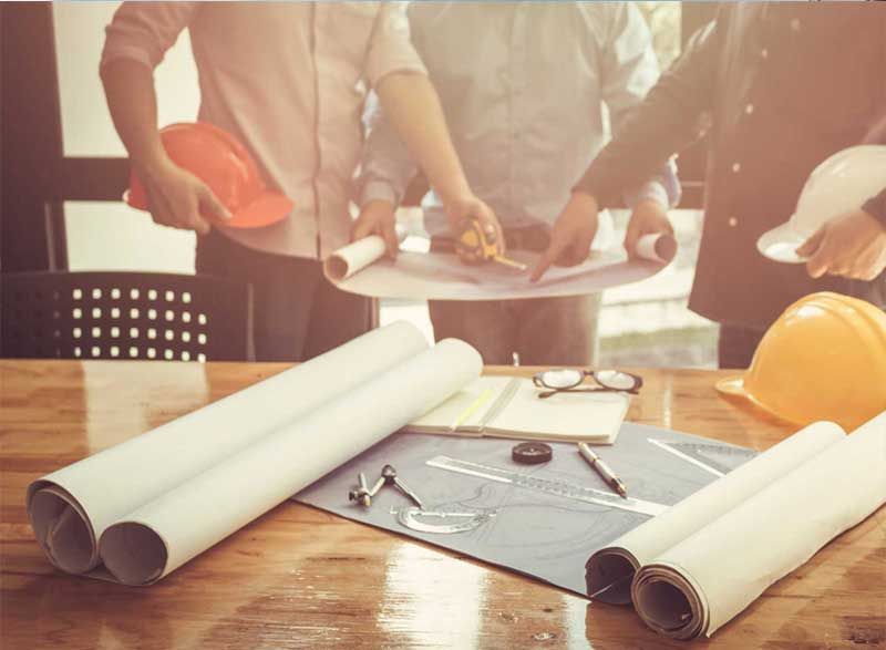 a group of construction workers are looking at blueprints on a wooden table .