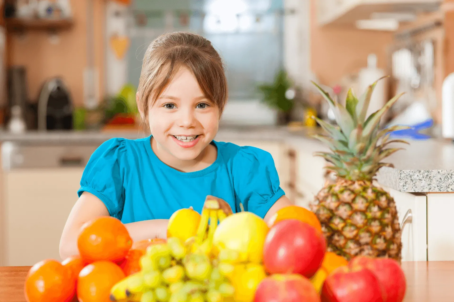 Une petite fille est assise à une table avec un bol de fruits.