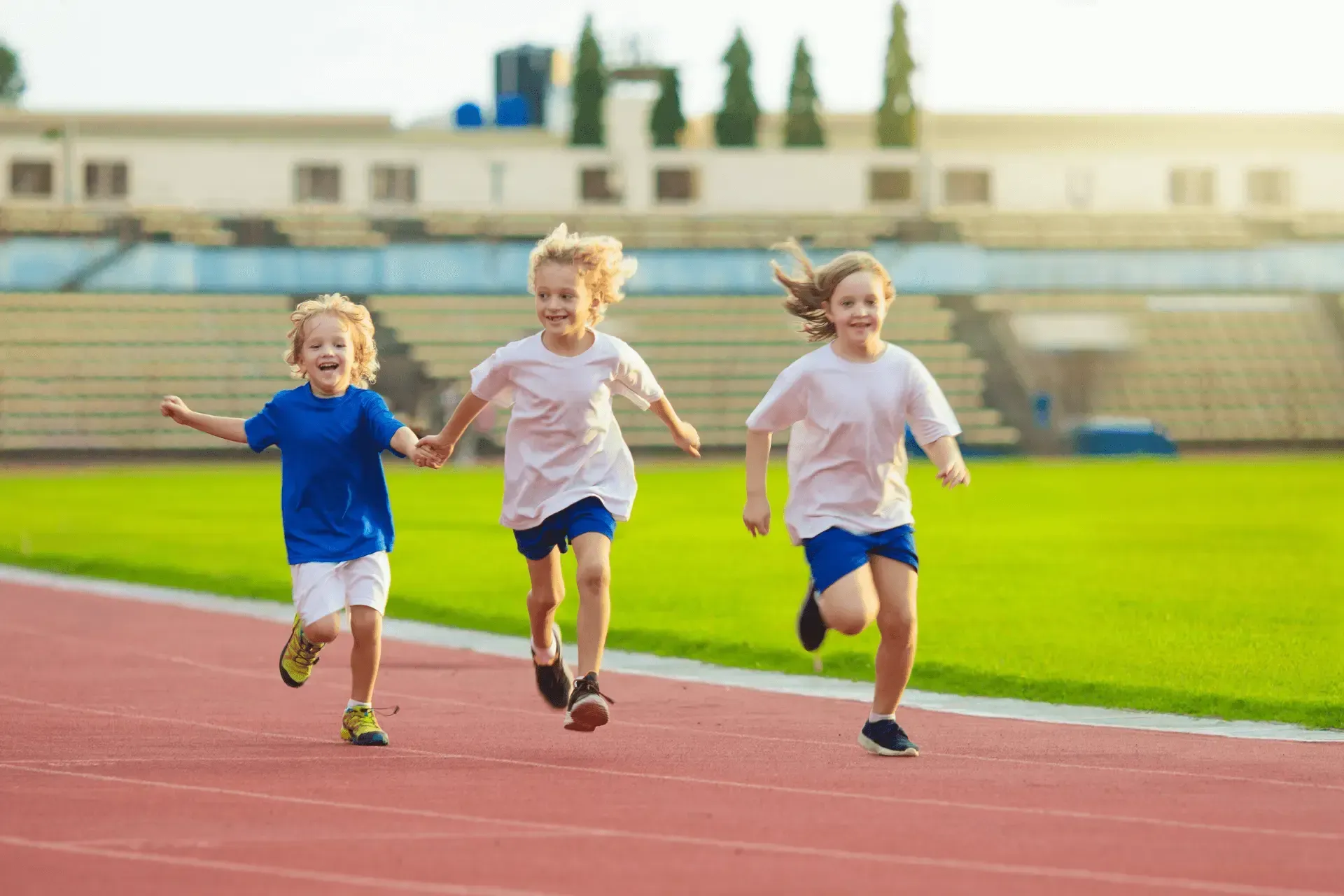 Trois enfants courent sur une piste dans un stade.