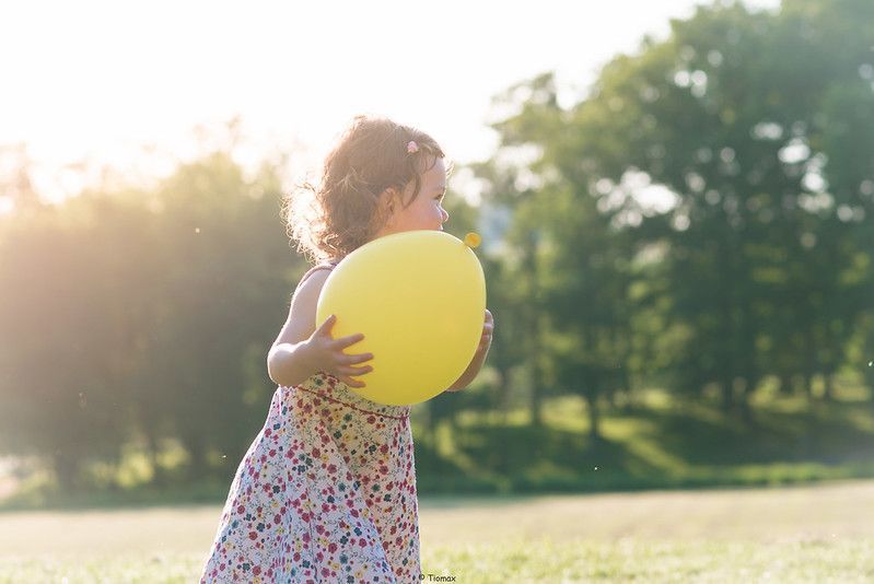 Young child in floral dress holds yellow balloon in sunny park.