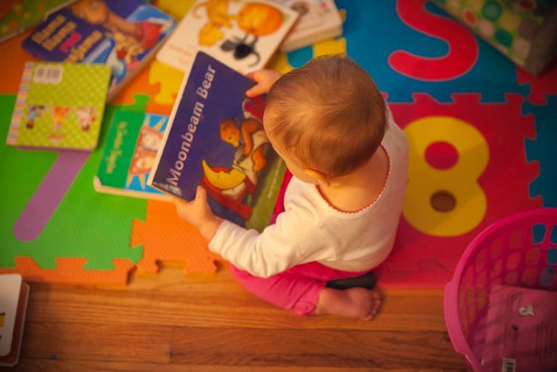 Toddler sitting on colorful mat, reading 