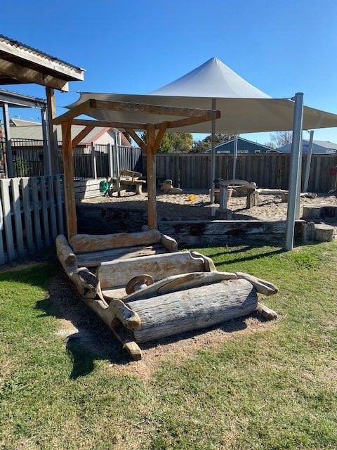 Playground with wooden cart, sandbox, and shade structure.