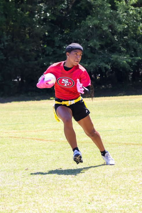 flag football player in a red shirt and black shorts running on a grassy field with a yellow flag belt