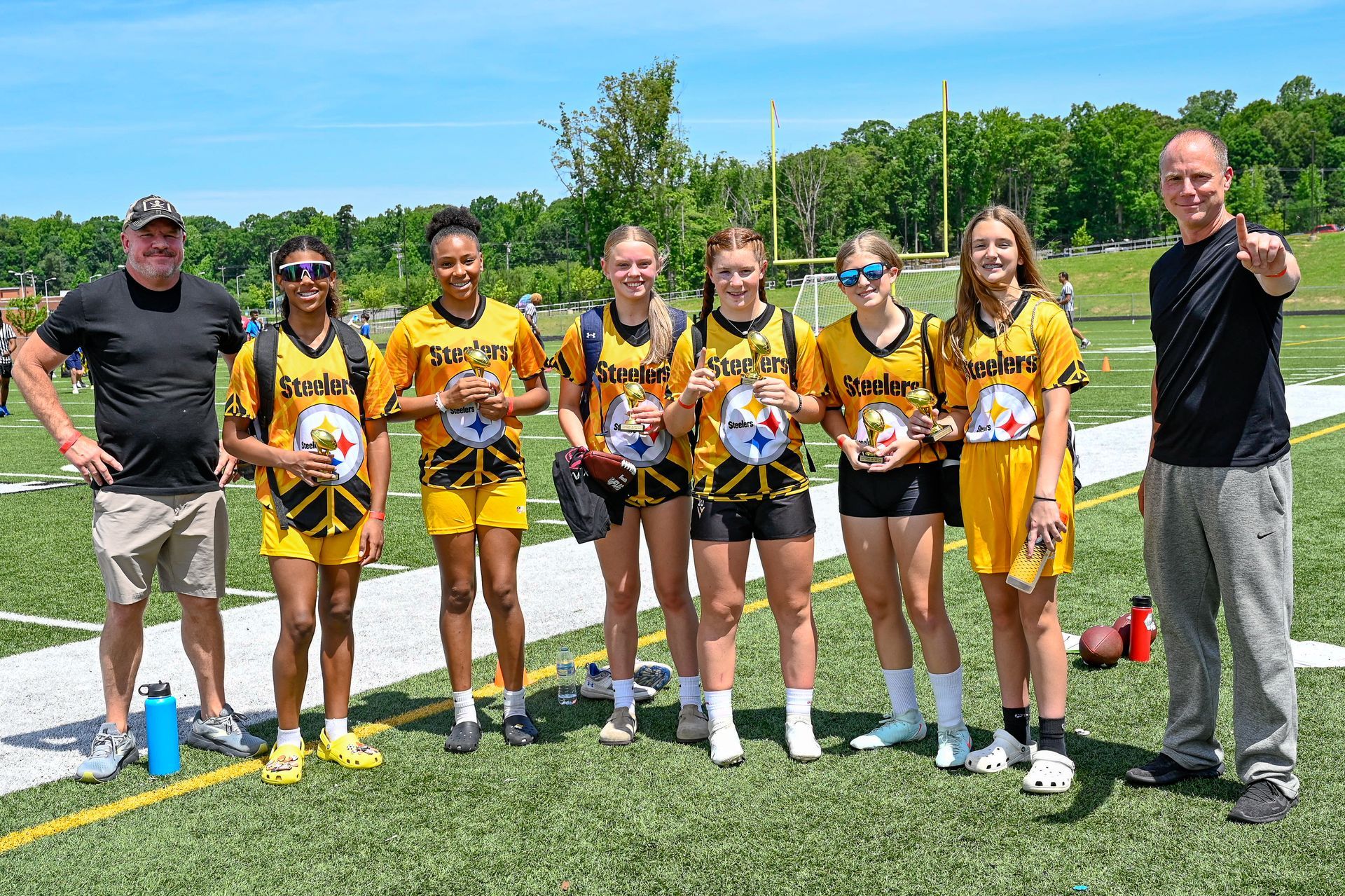 Seven flag football athletes in yellow uniforms posing on a sports field with a ball under a blue sky