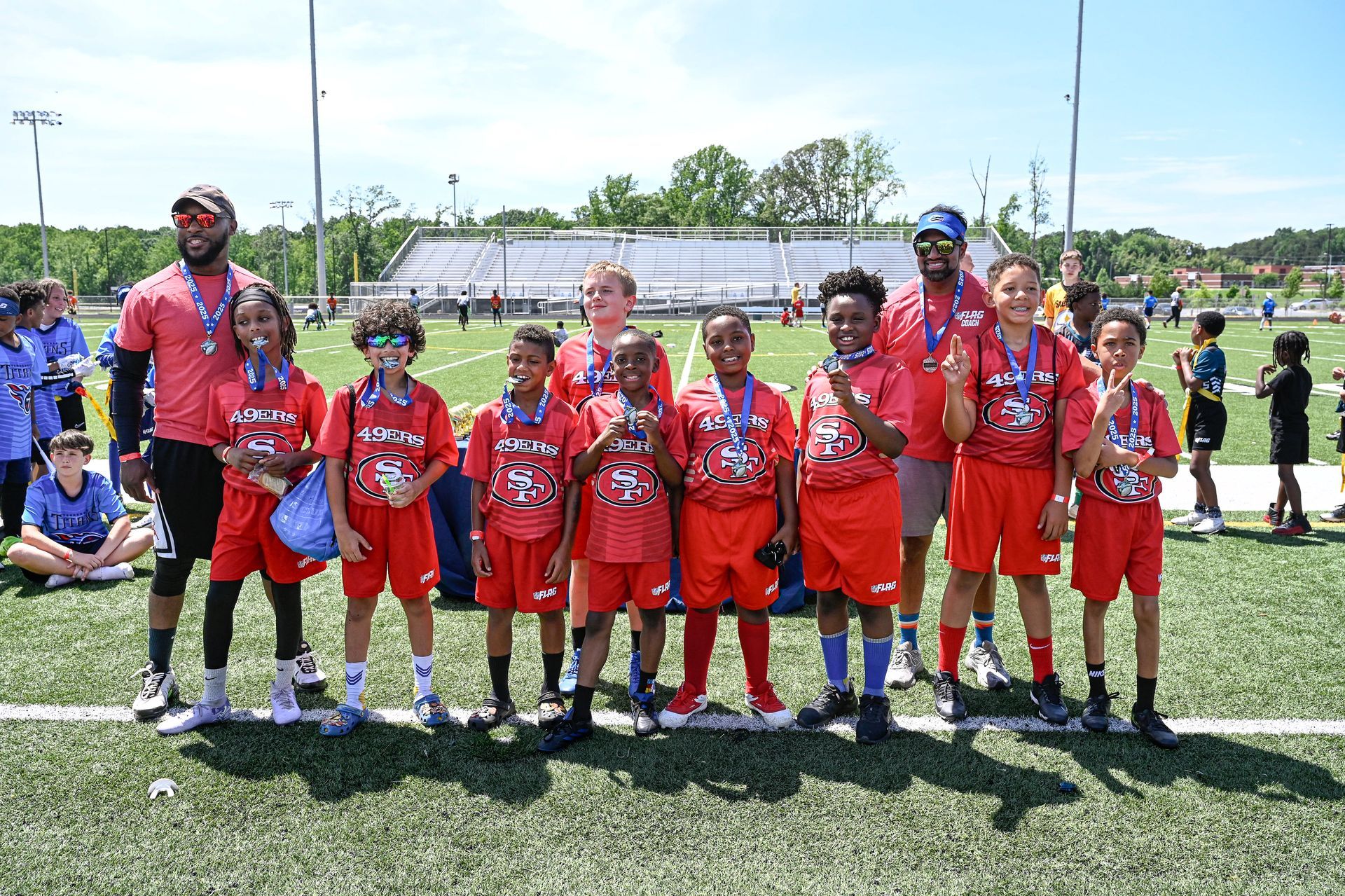 Flag Football team posing for a group photo on a field, wearing red uniforms, with a coach standing at the side