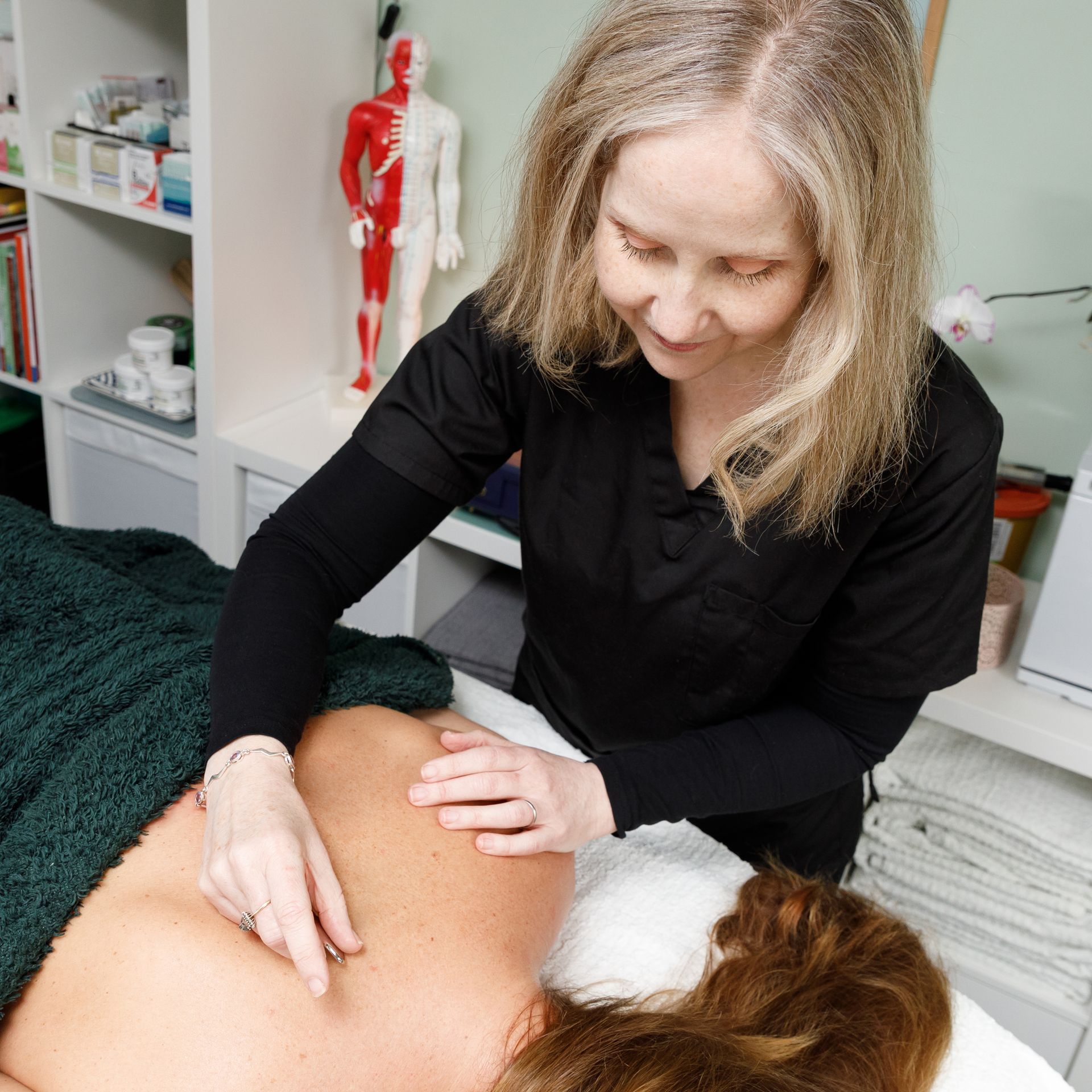 Woman performing massage on a client's back in a treatment room.