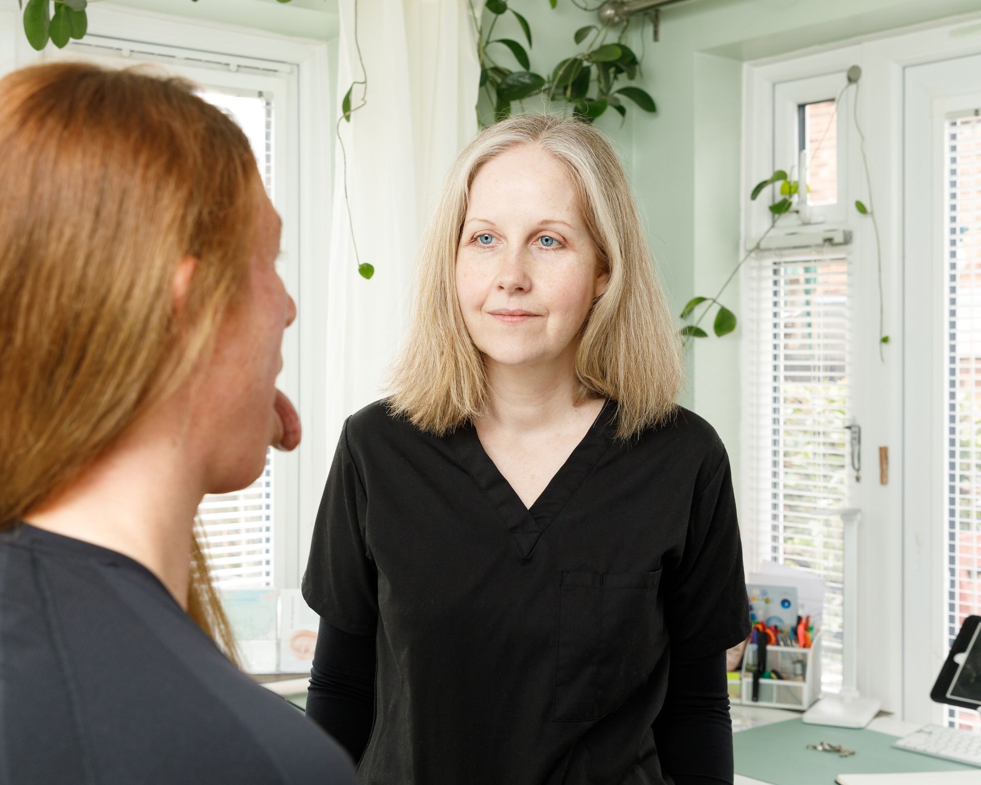 A healthcare professional examines a patient's open mouth, indoors.