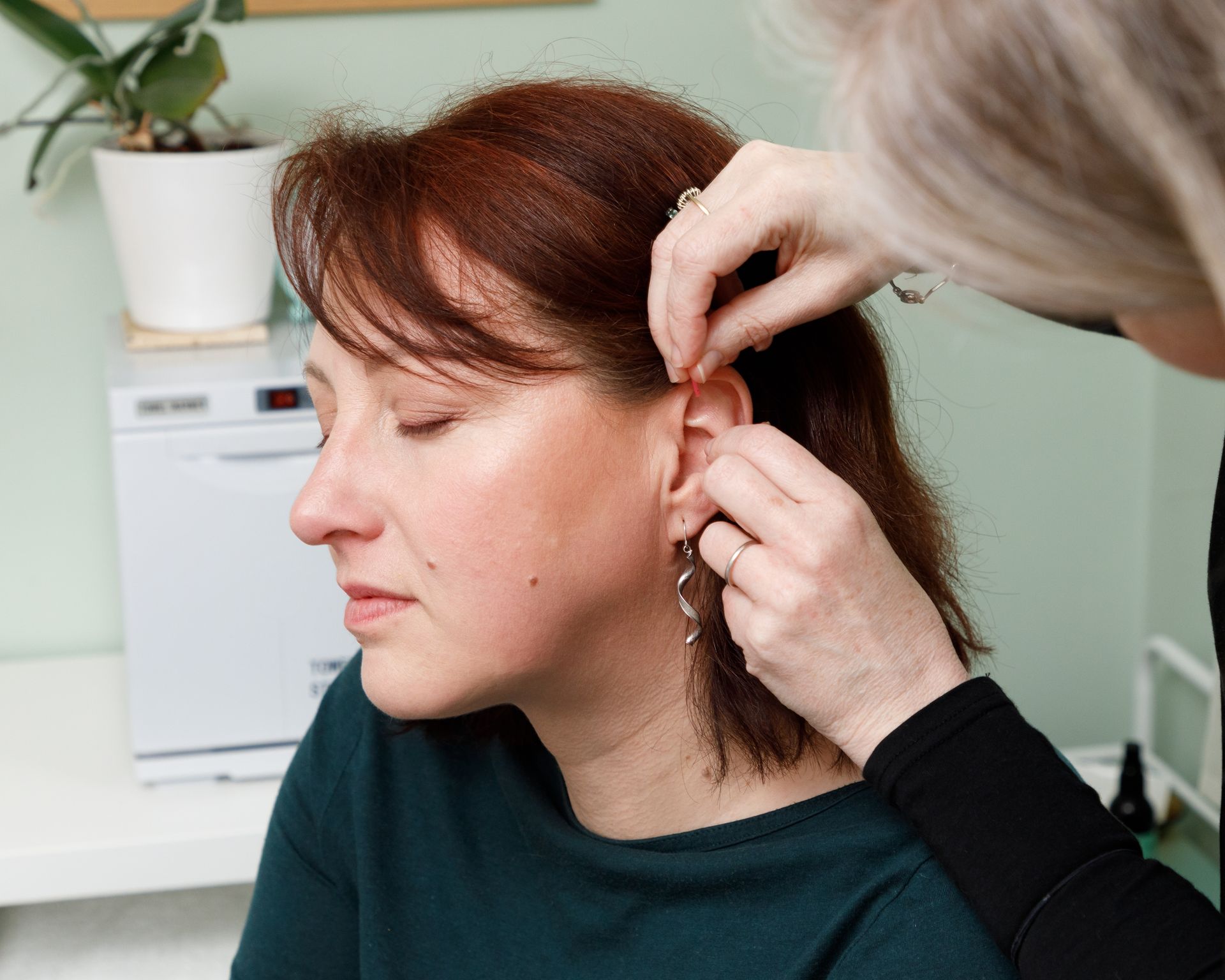 Woman having earring adjusted by another person. Indoor setting.