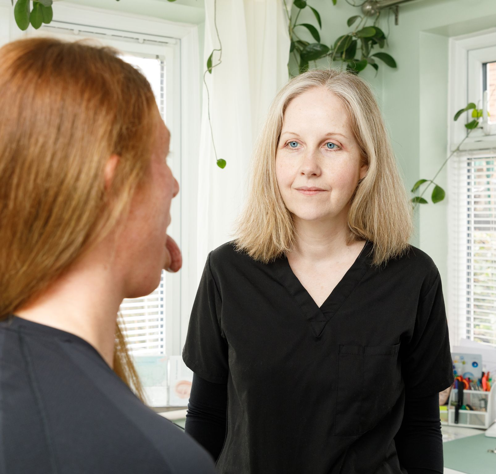 A healthcare professional examines a patient's open mouth, indoors.