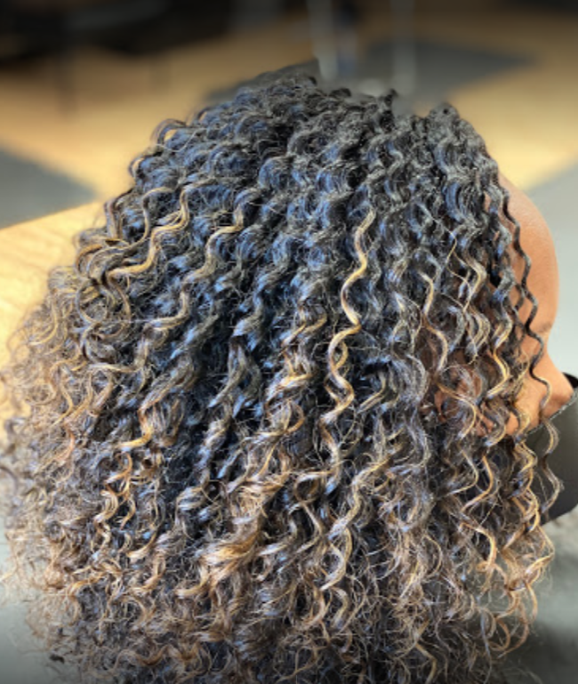 Woman with dark curly hair, highlighted with blonde, in a salon setting.