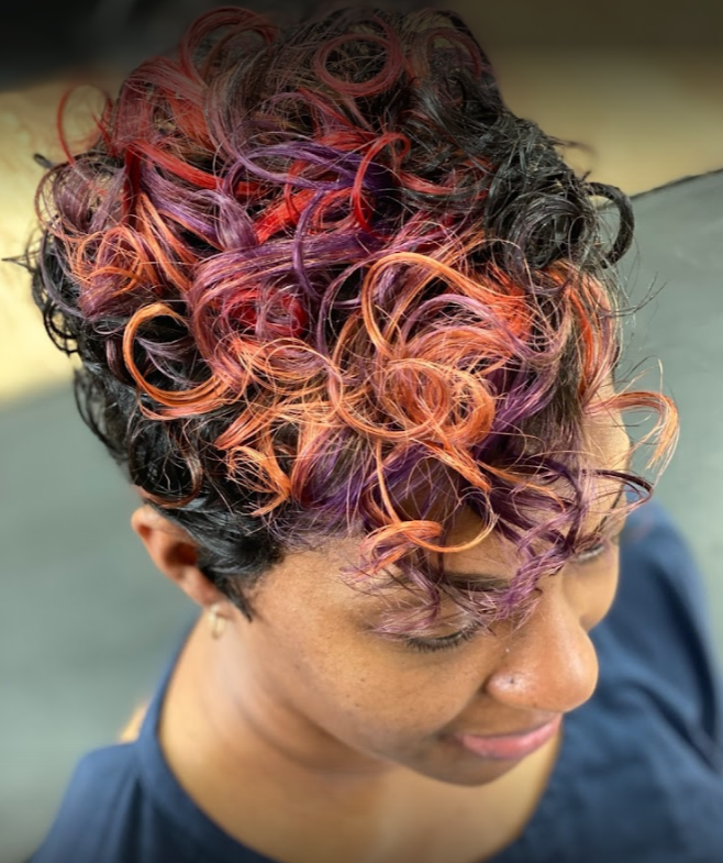Woman with short, curly hair dyed black with red, orange, and purple highlights.