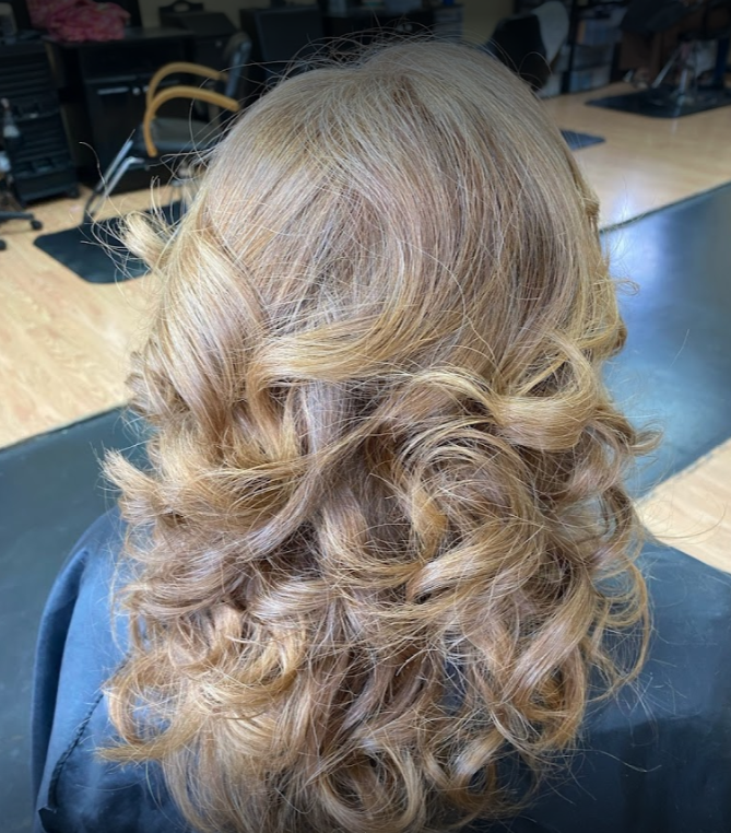 Woman with light brown, curly hair styled in voluminous waves at a salon.