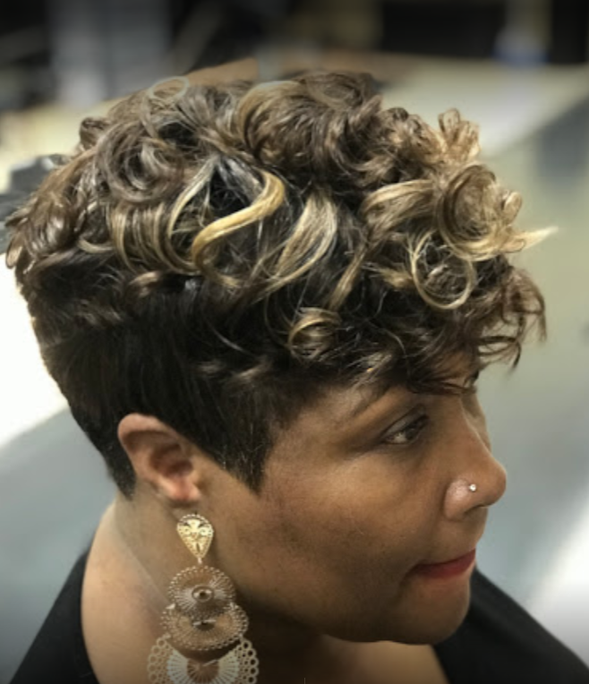 Woman with short, curly hair, side profile. Dark hair with blonde highlights, wearing earrings.