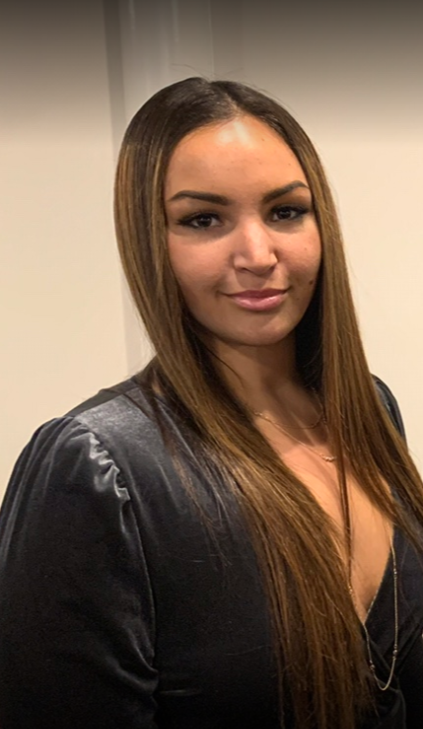Woman with long brown hair and a dark top, smiling at the camera.
