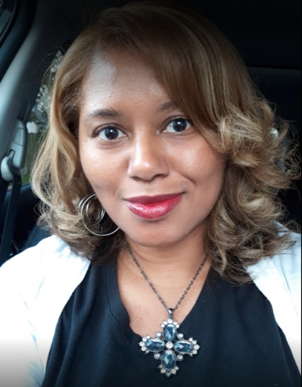 Woman with light brown hair and a cross necklace smiling in a car.