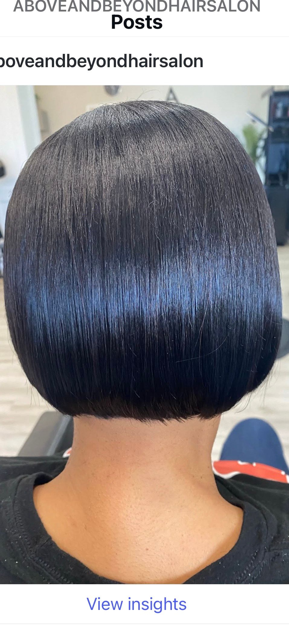 Back view of person with a short, sleek, black bob haircut, sitting in a salon chair.