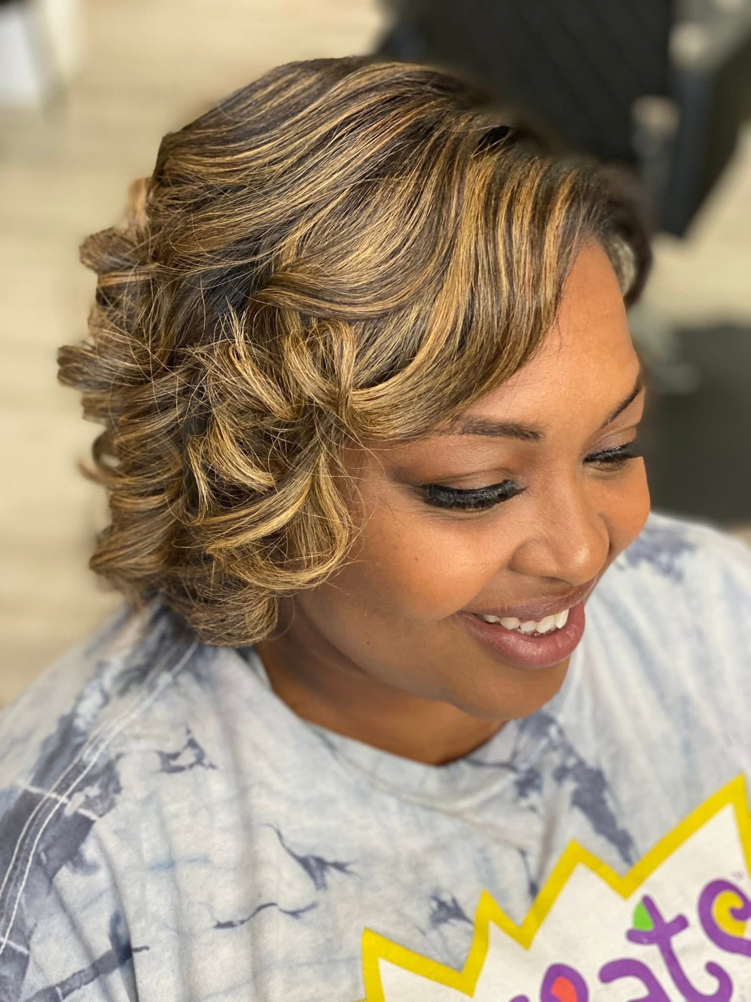 Woman with curly brown and blonde highlighted hair smiles, wearing a tie-dye shirt.