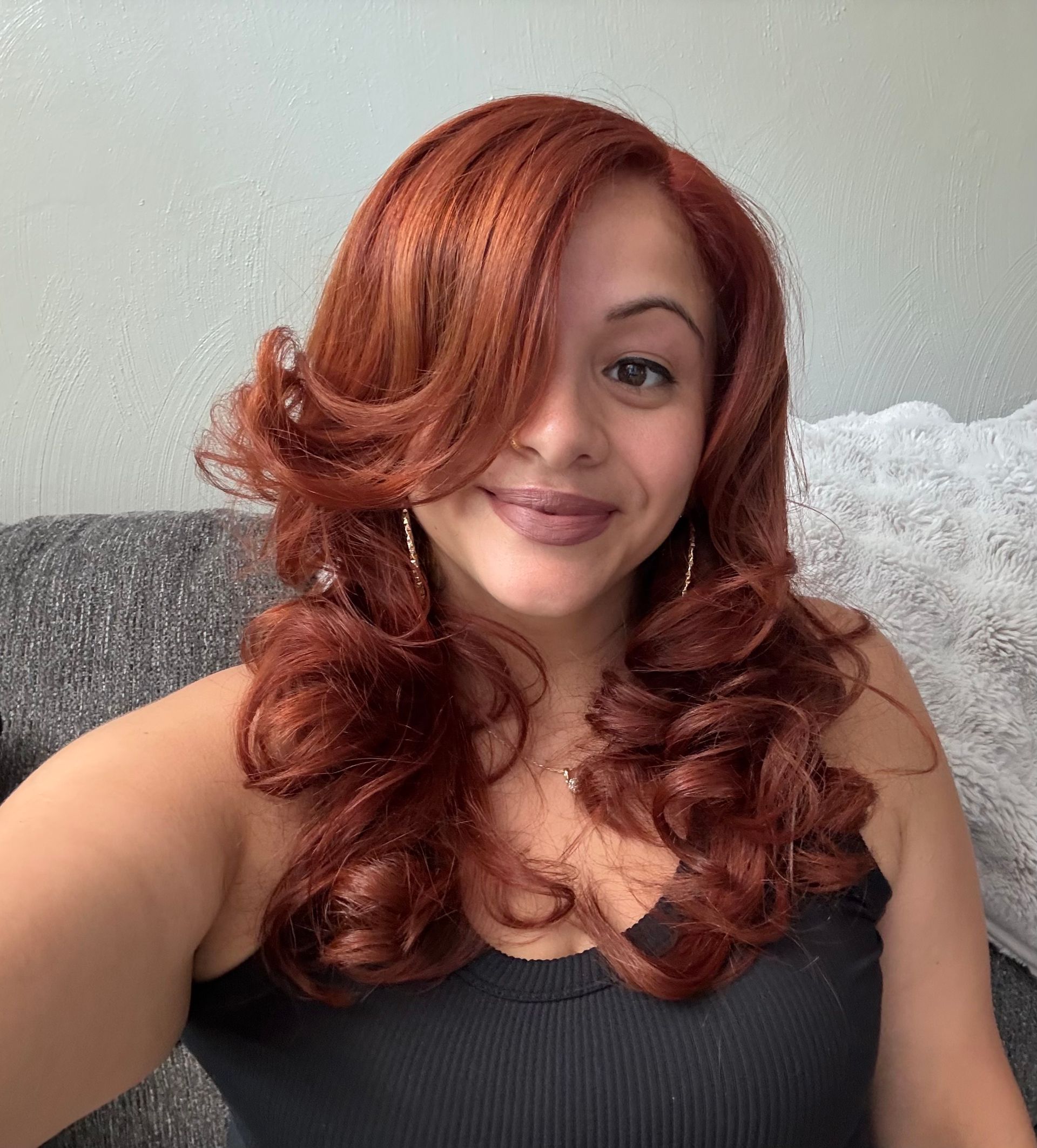 Woman with auburn hair, wearing a black tank top, smiling at the camera.