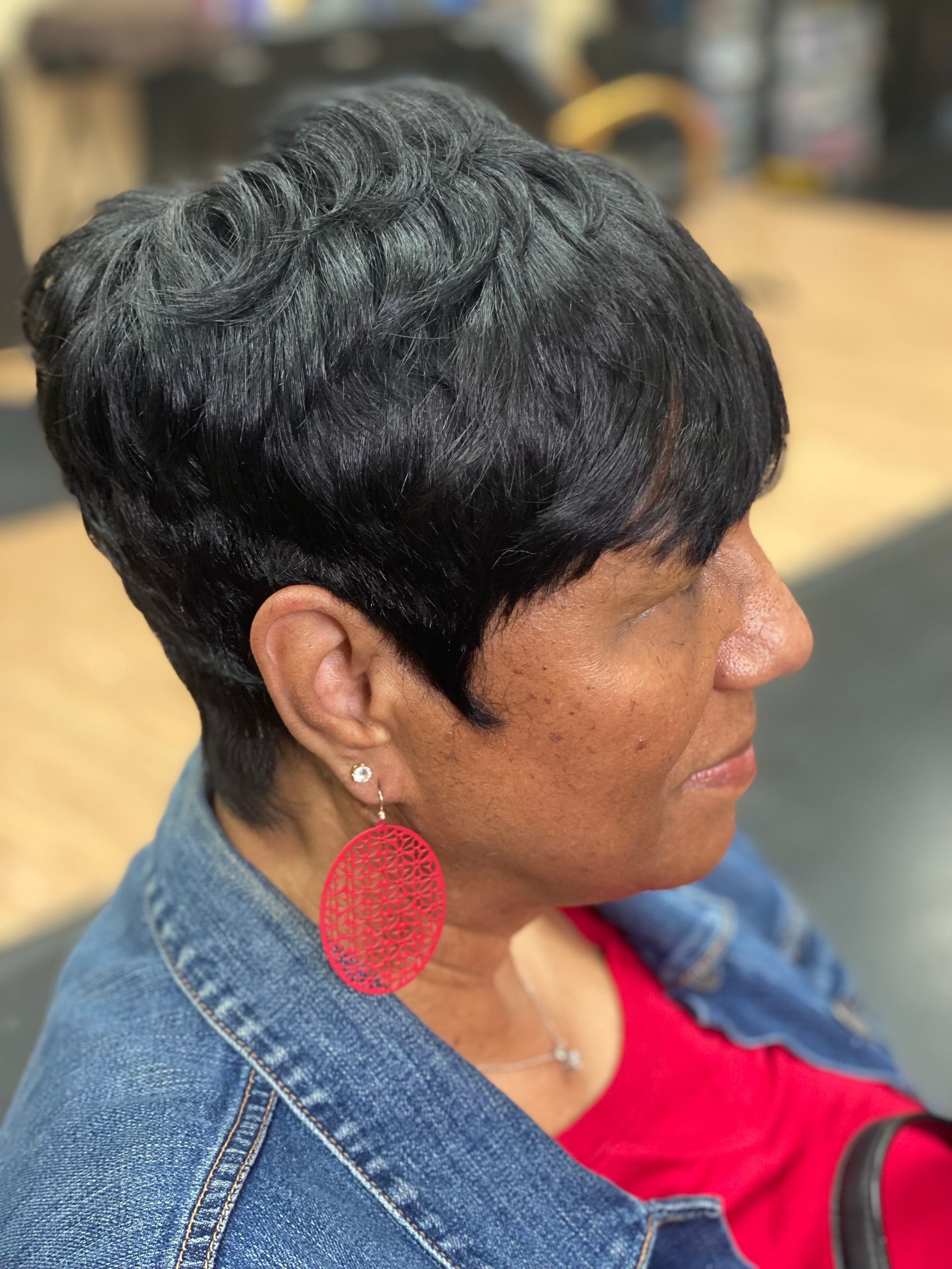 Woman with short black hair, wearing a red top, denim jacket, and red earrings.