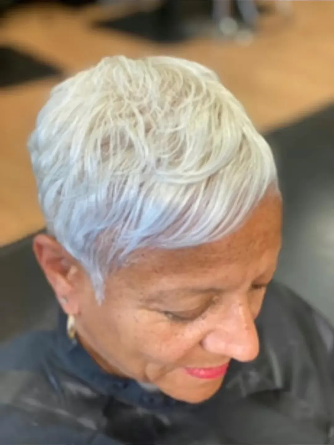 Woman with short, styled silver hair and red lipstick, sitting in a salon.