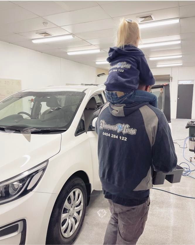 A Man is Carrying a Child on His Shoulders in Front of a White Car — Diamond Tints In Goulburn, ACT
